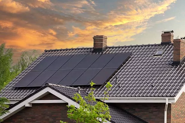 Auf dem Dach eines Hauses ist eine Photovoltaikanlage. Im Hintergrund sieht man den Sonnenuntergang.